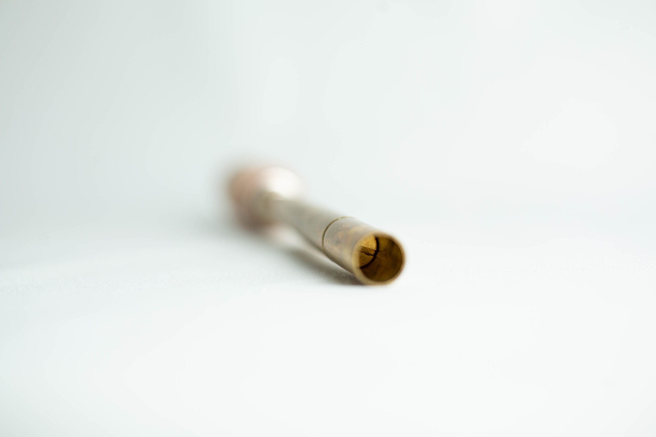 A brass tube with a slightly flared end, lying on a white surface, focussed on the open tip.
