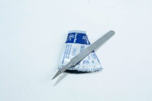 A metal scalpel rests on top of a blue and white sterile packaging on a white surface.