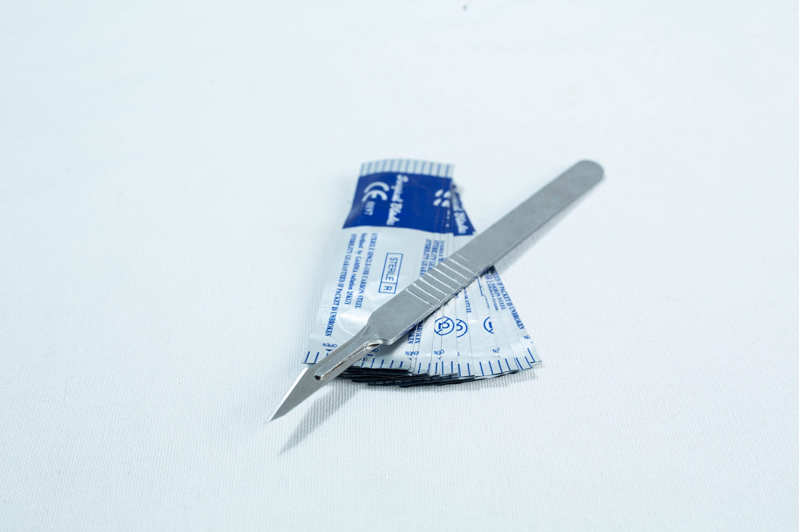 A metal scalpel rests on top of a blue and white sterile packaging on a white surface.