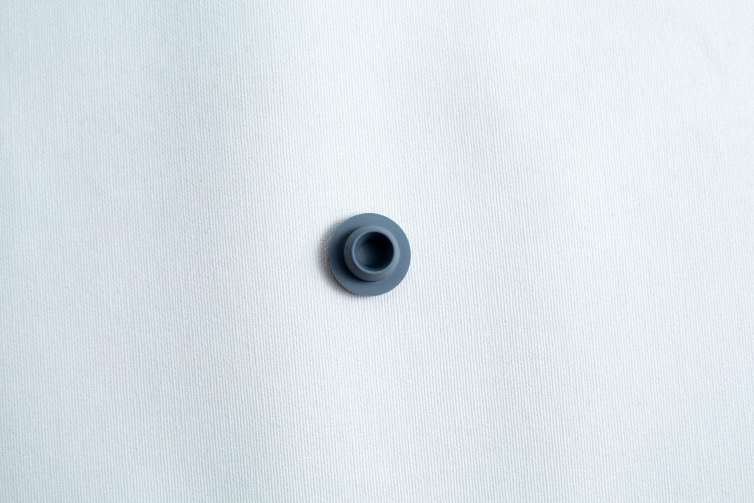 A single dark grey button on a plain white textured fabric background.
