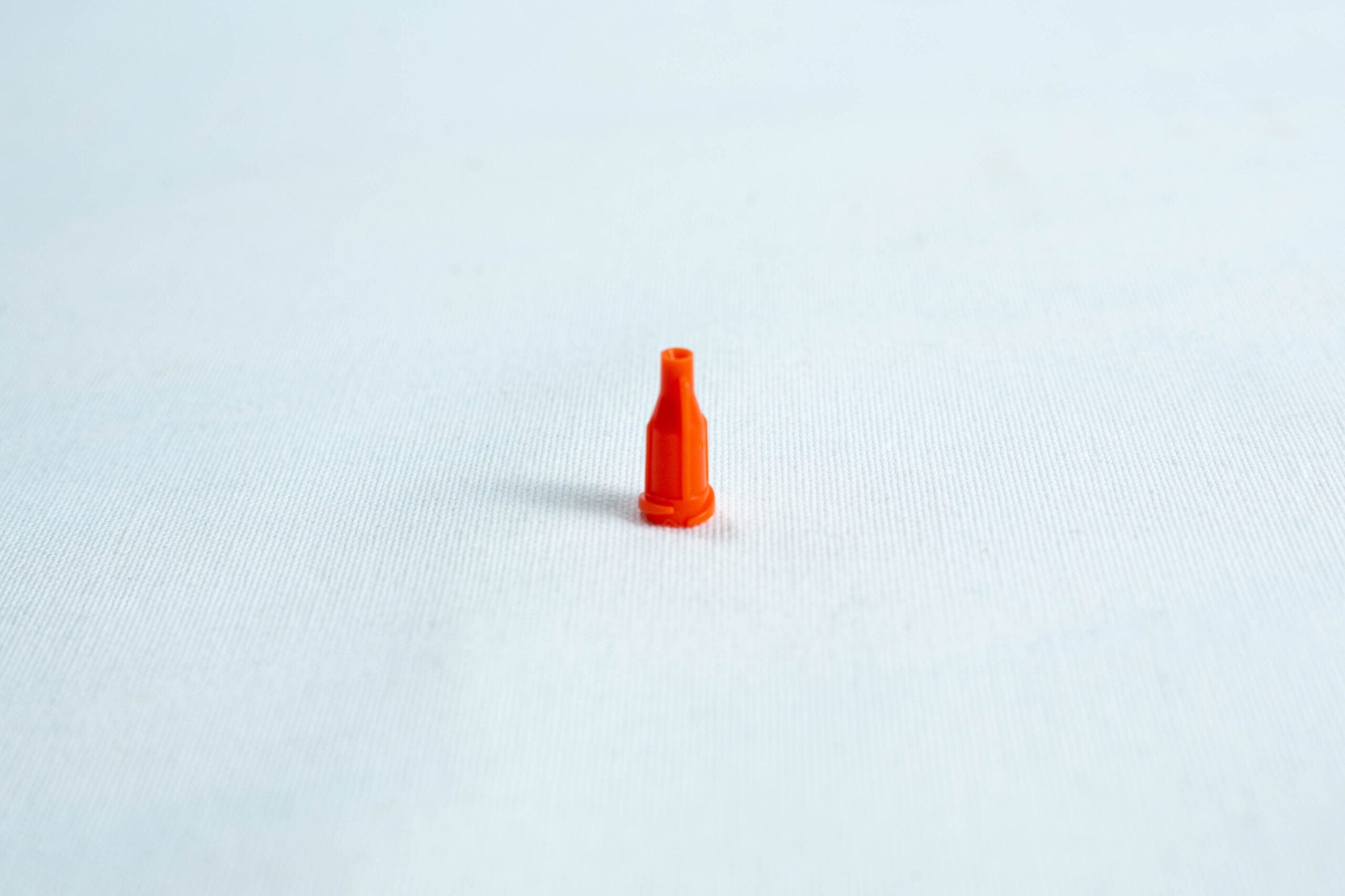 A small orange plastic nozzle stands upright on a plain white surface.