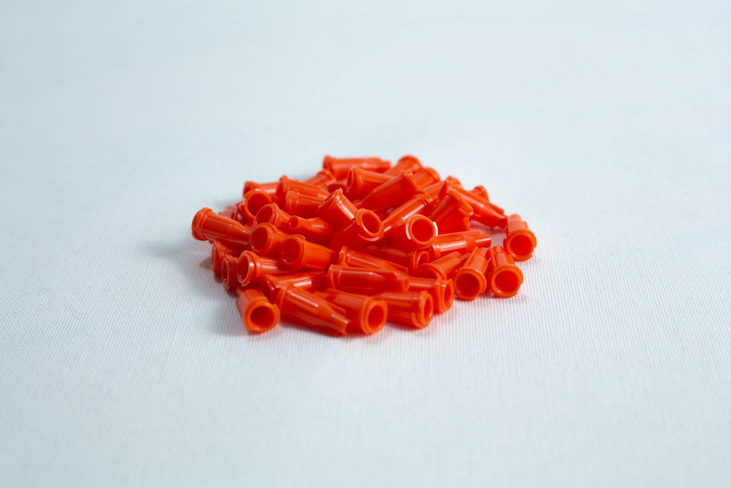 A pile of small, orange plastic caps on a white surface.