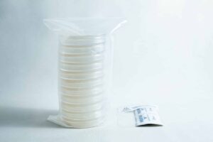 A stack of sealed petri dishes and a small packet on a white surface with a plain background.