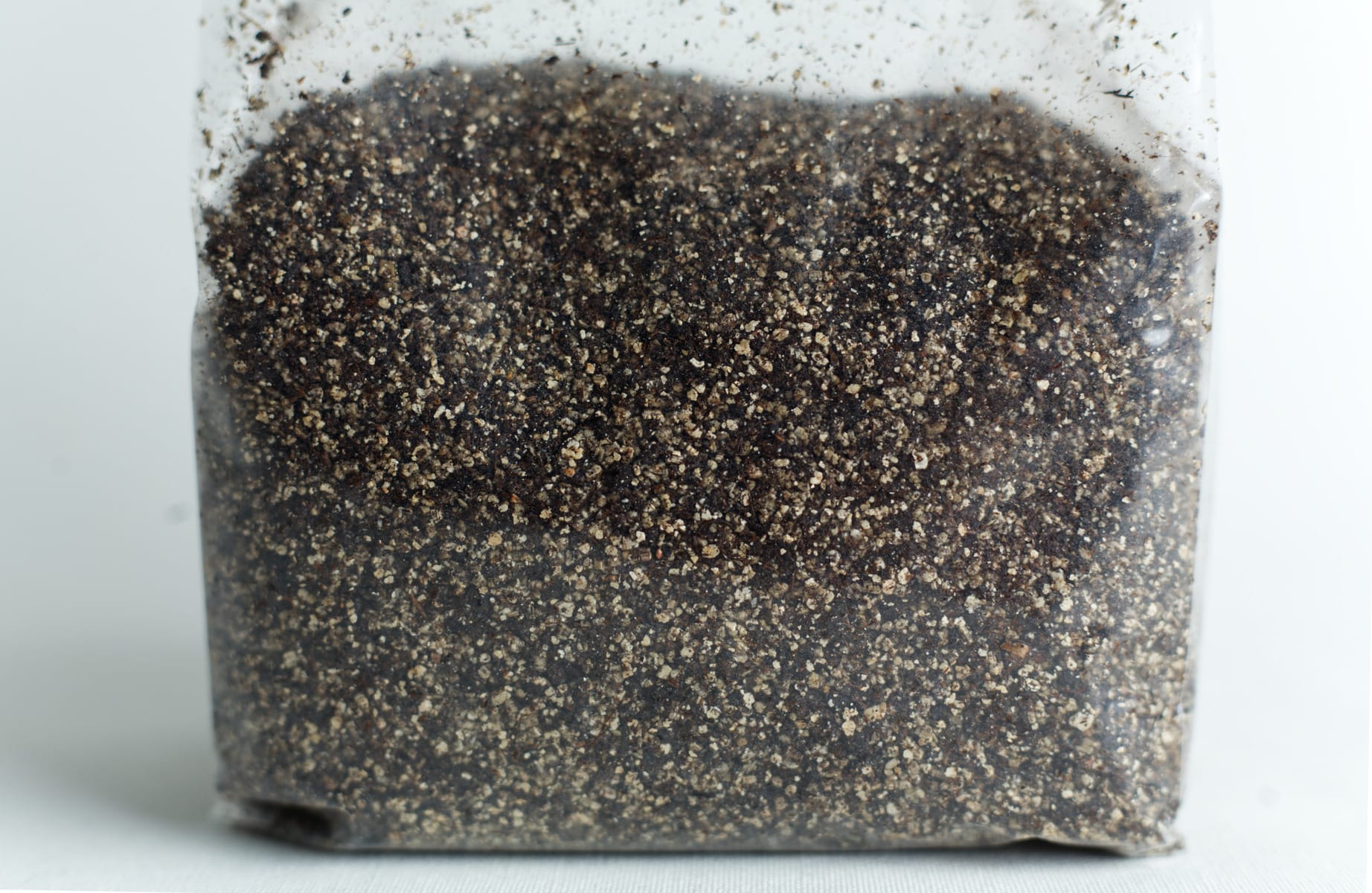 A clear plastic bag filled with coarse, dark soil or sand on a white surface.