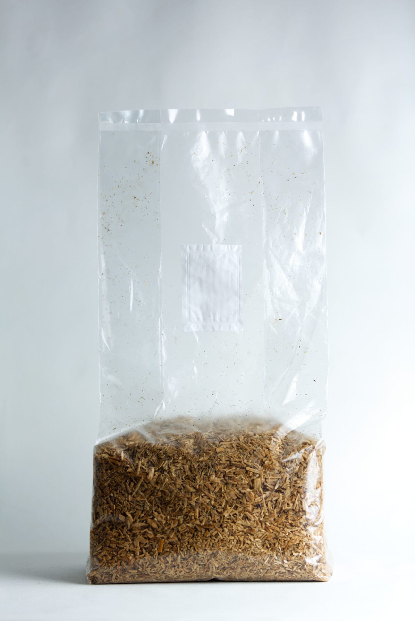A clear plastic bag filled with brown woodchips against a plain white background.