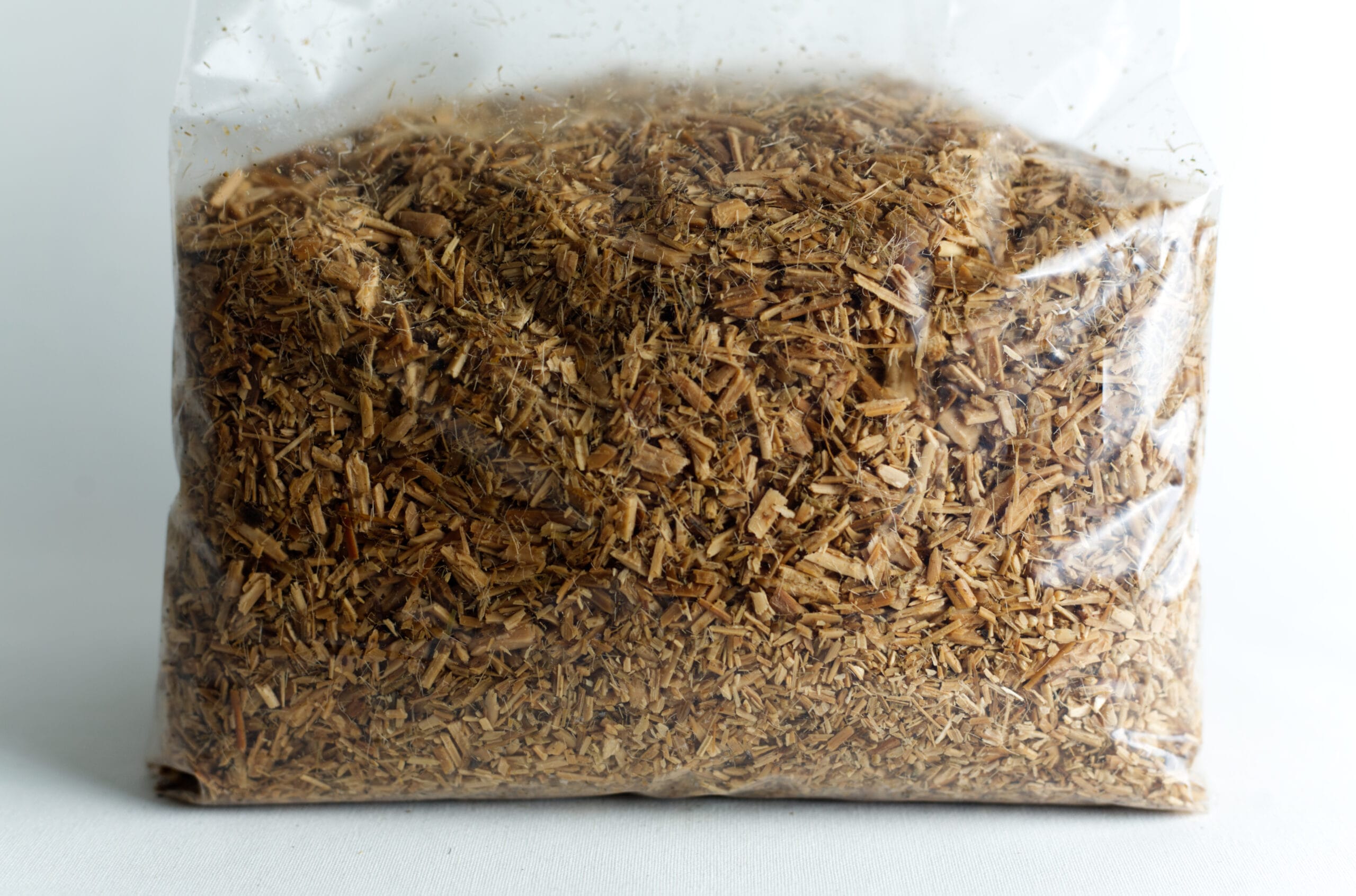 A clear plastic bag filled with chopped wood chips or shavings against a white background.