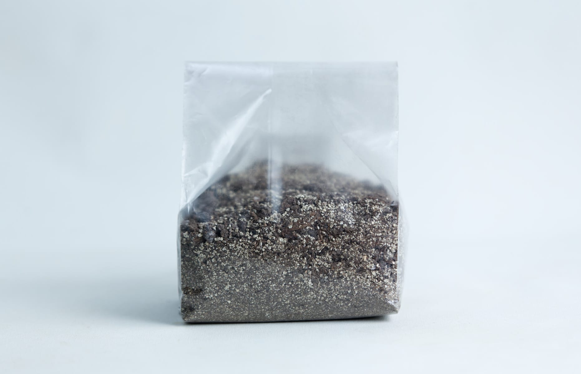 A clear plastic bag filled with sand and small pebbles, set against a plain white background.