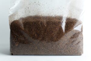 Clear plastic bag filled with brown ground coffee against a white background.