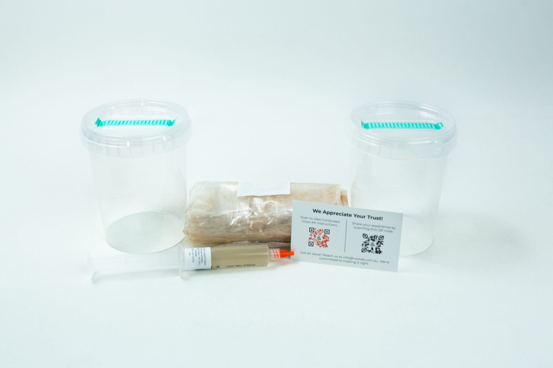 Two empty plastic containers, a wrapped item, syringe, and info card from the Cordyceps militaris Mushroom Grow Kit are arranged on a white background.