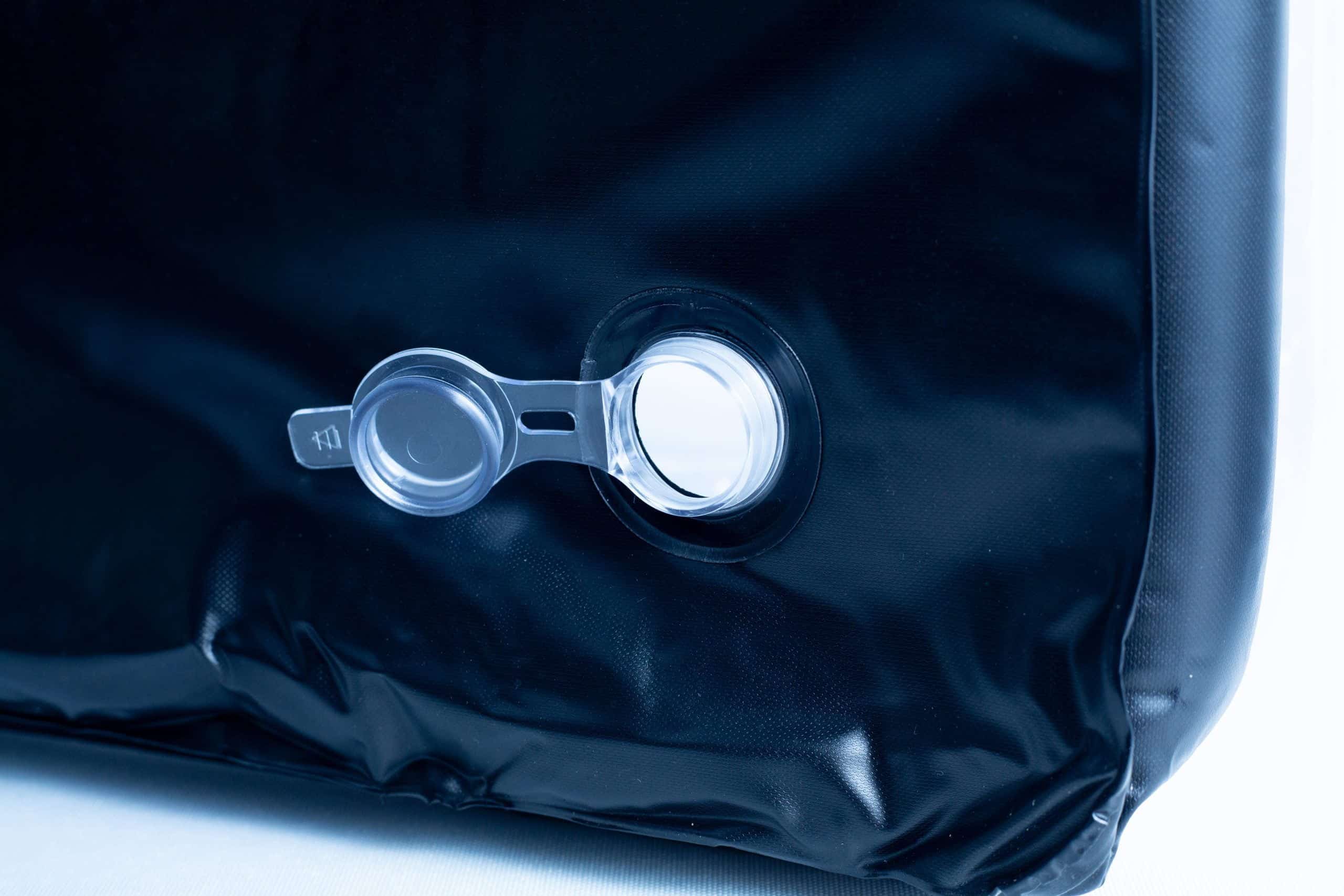 Close-up of an air valve on a black inflatable object, with a transparent plastic cap.