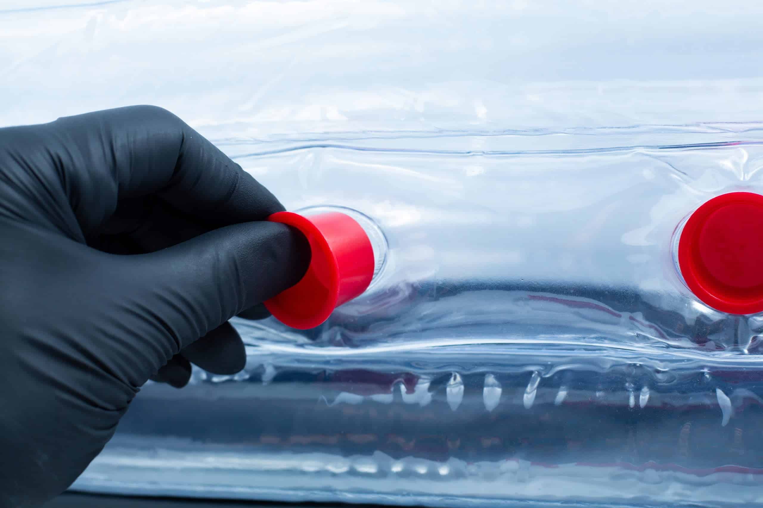 Gloved hand opening a red cap on a clear plastic inflatable or medical isolation chamber.