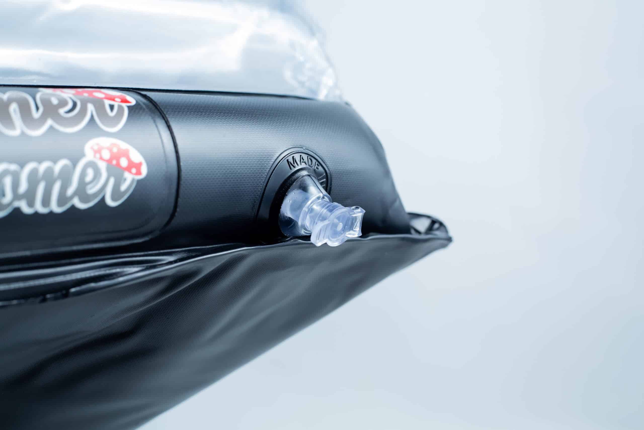 Close-up of an air valve on a black inflatable object with some stickers nearby.