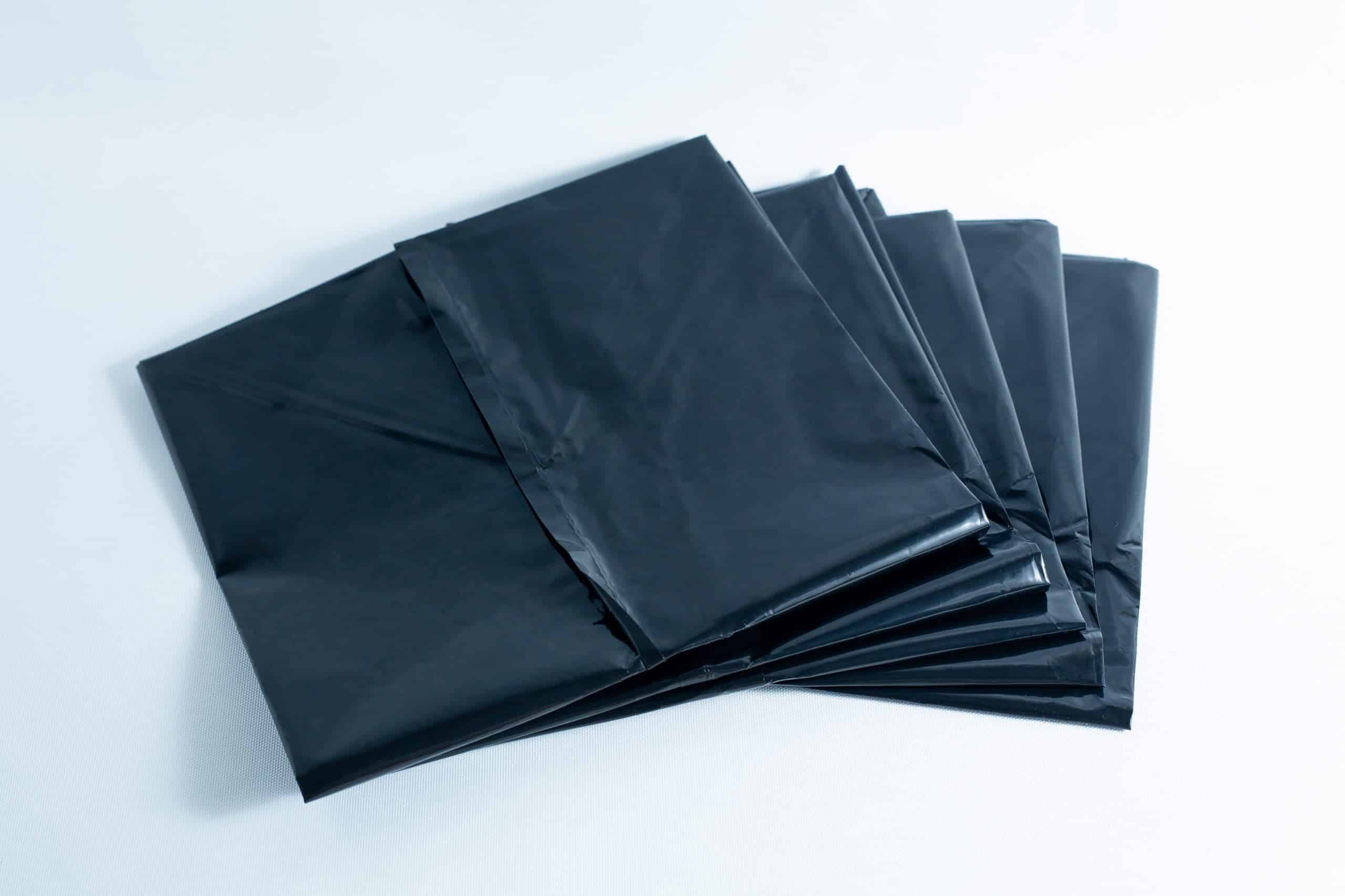 A stack of black plastic bin bags laid out on a white surface.