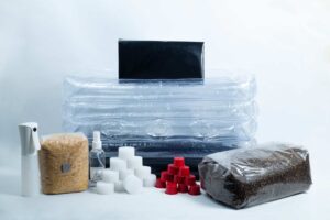 Mushroom growing kit with a plastic tent, substrate bag, spray bottle, sponges, and red caps.