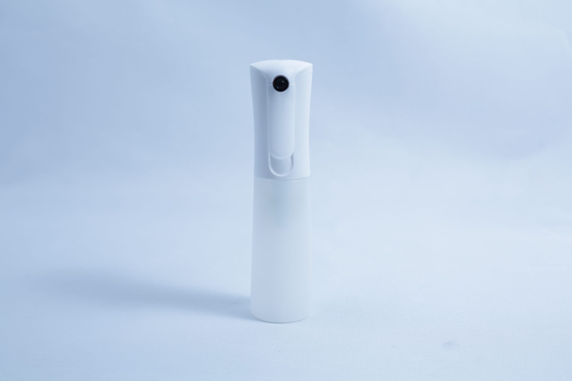 A white plastic spray bottle, ideal for use with the Monotub Mushroom Growing Kit-Premium, stands upright on a plain light blue background.