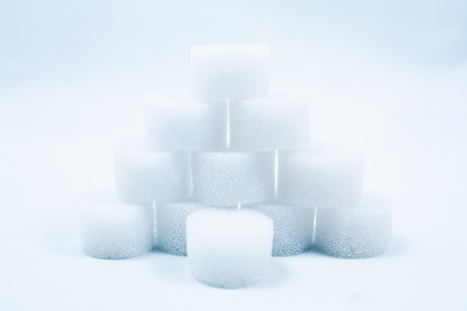 A pyramid of white, round foam sponges stacked on a white surface with a soft, light background.