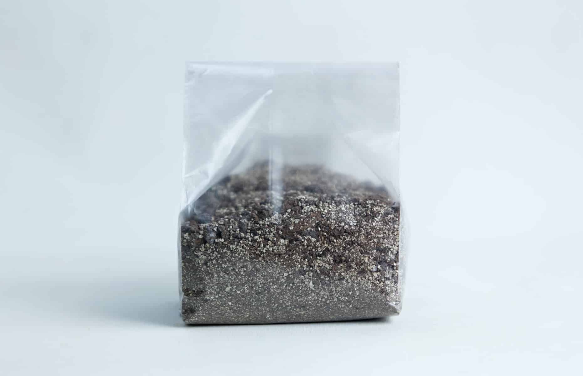 A clear plastic bag filled with a mixture of small, dark and light grains—perfect for use with the Monotub Mushroom Growing Kit-Premium—set against a plain background.
