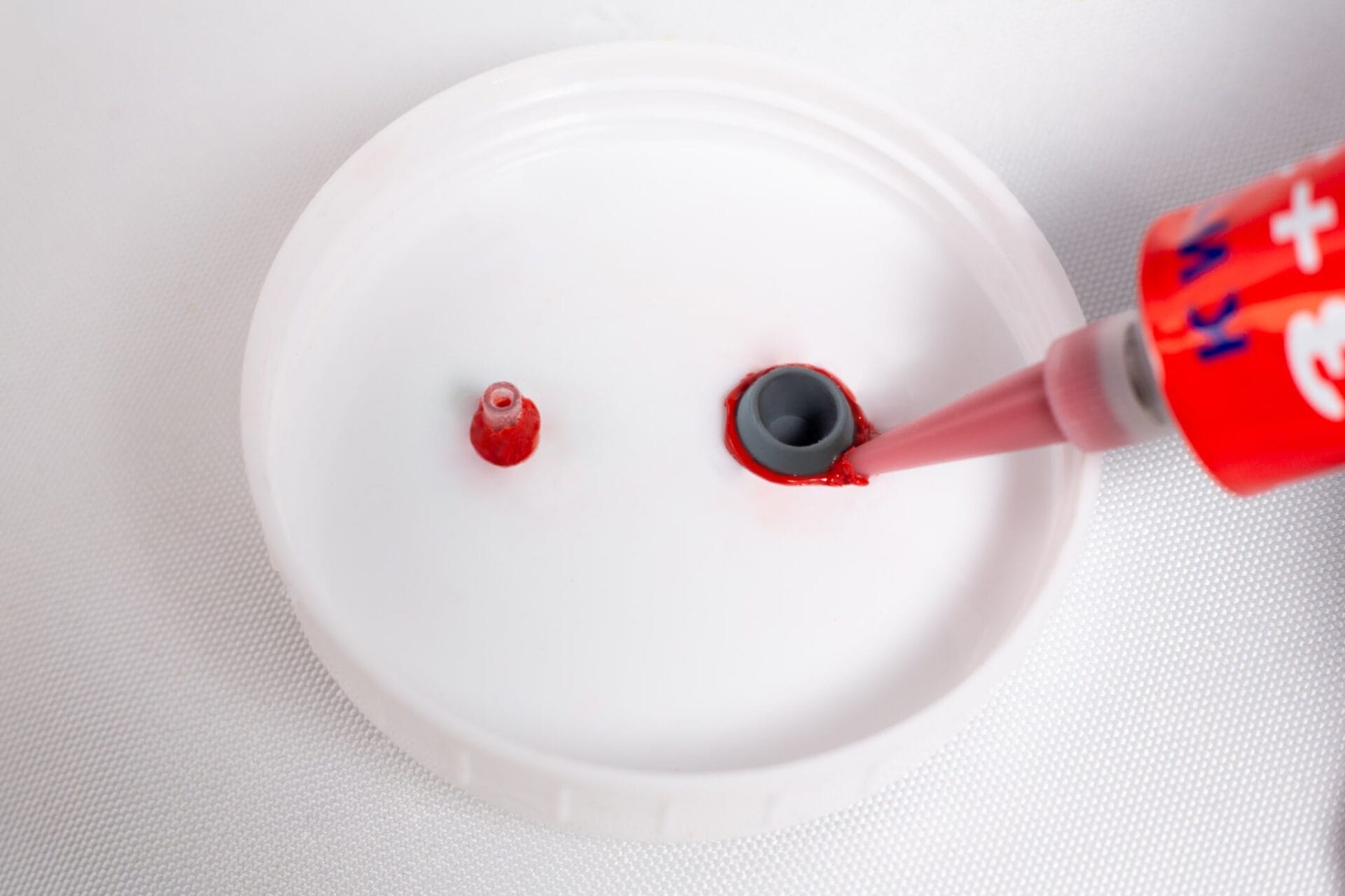 High Temperature RTV Silicone-Red is being applied around a grey nozzle on a white plastic surface.