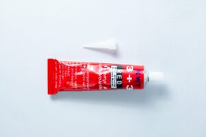 A red tube of High Temperature RTV Silicone-Red with a white cap placed above it on a white background.