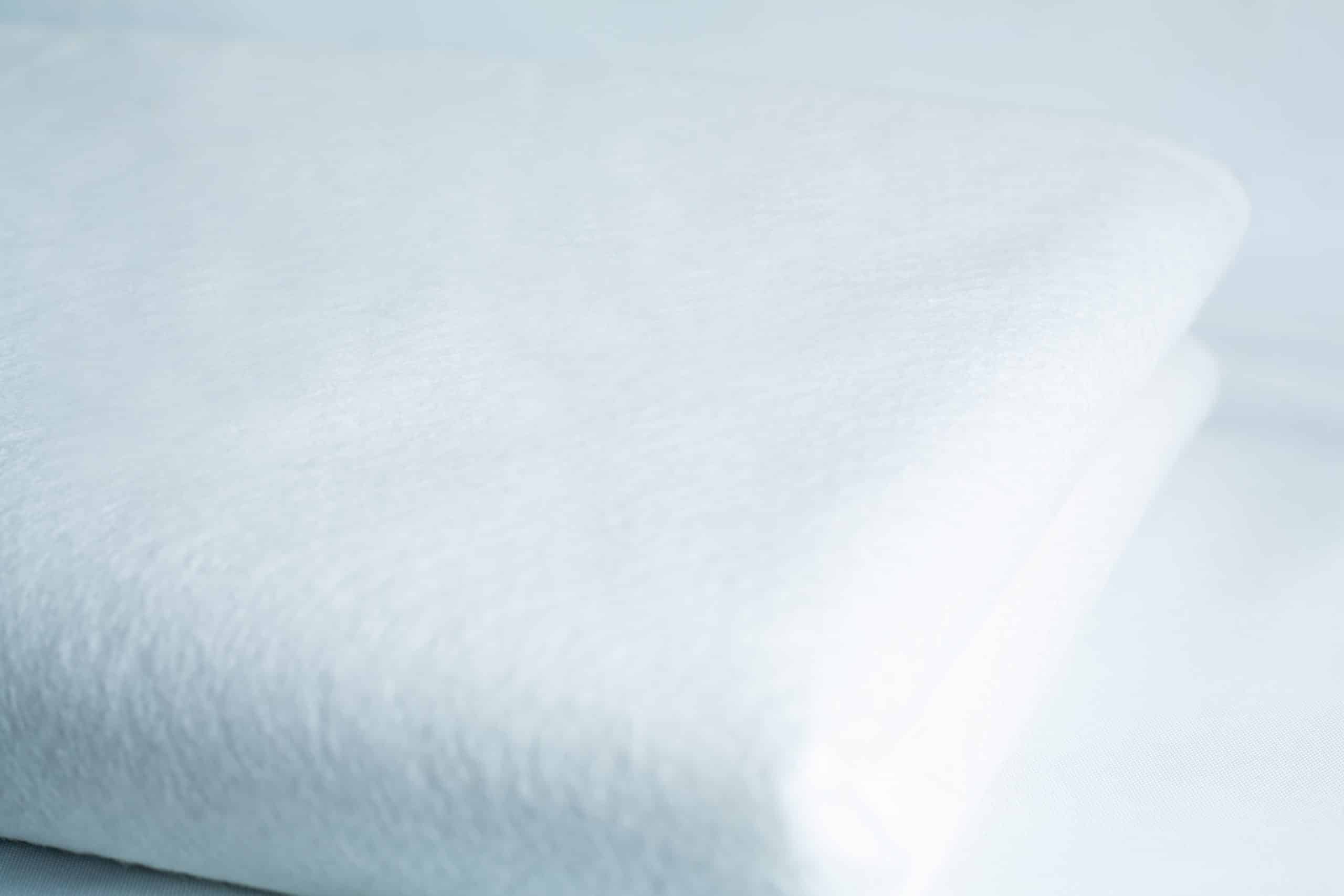 A close-up of a neatly folded white towel and the Light Log Blanket displayed on a white surface.