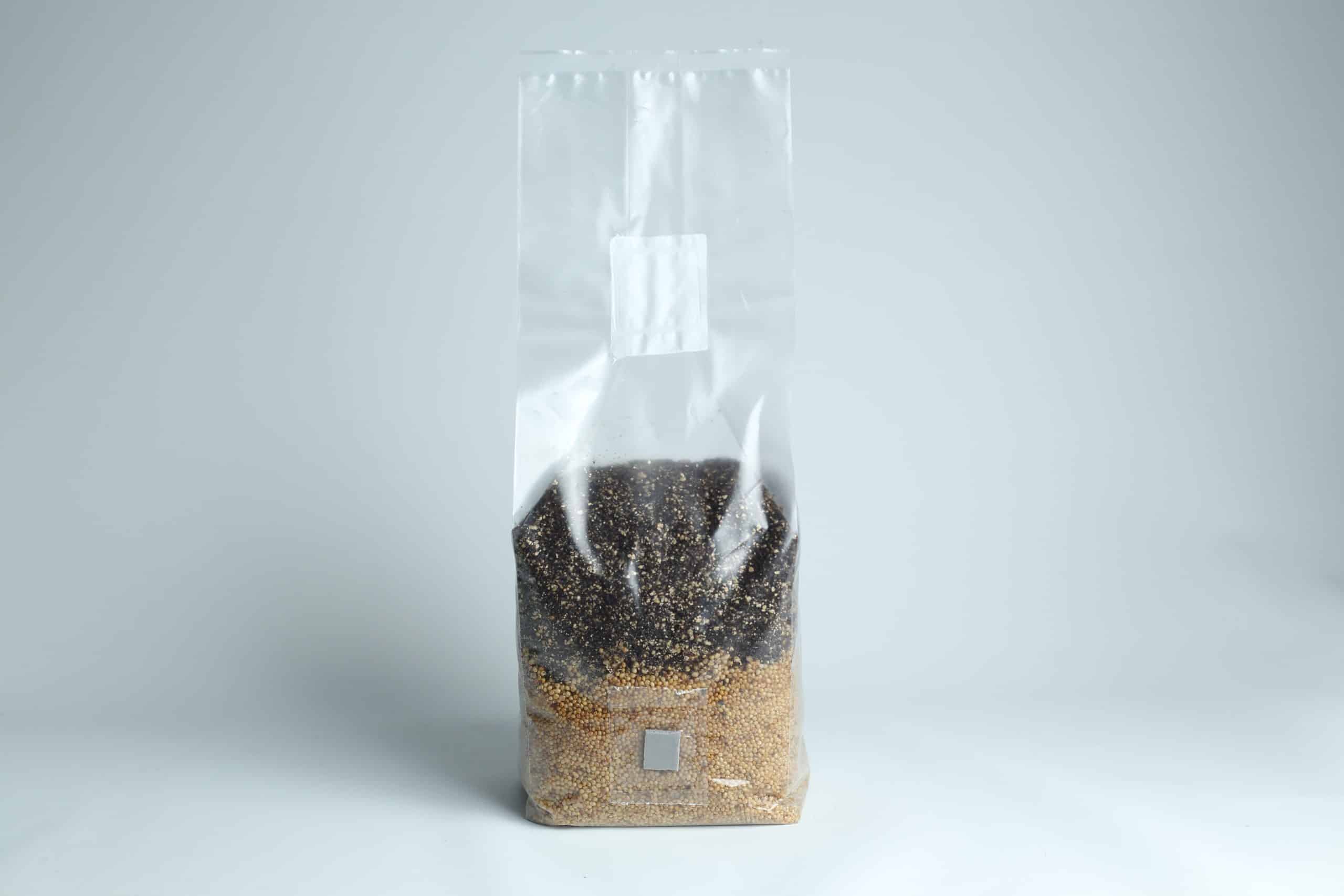 A clear plastic bag filled with black and brown grains on a plain white background.