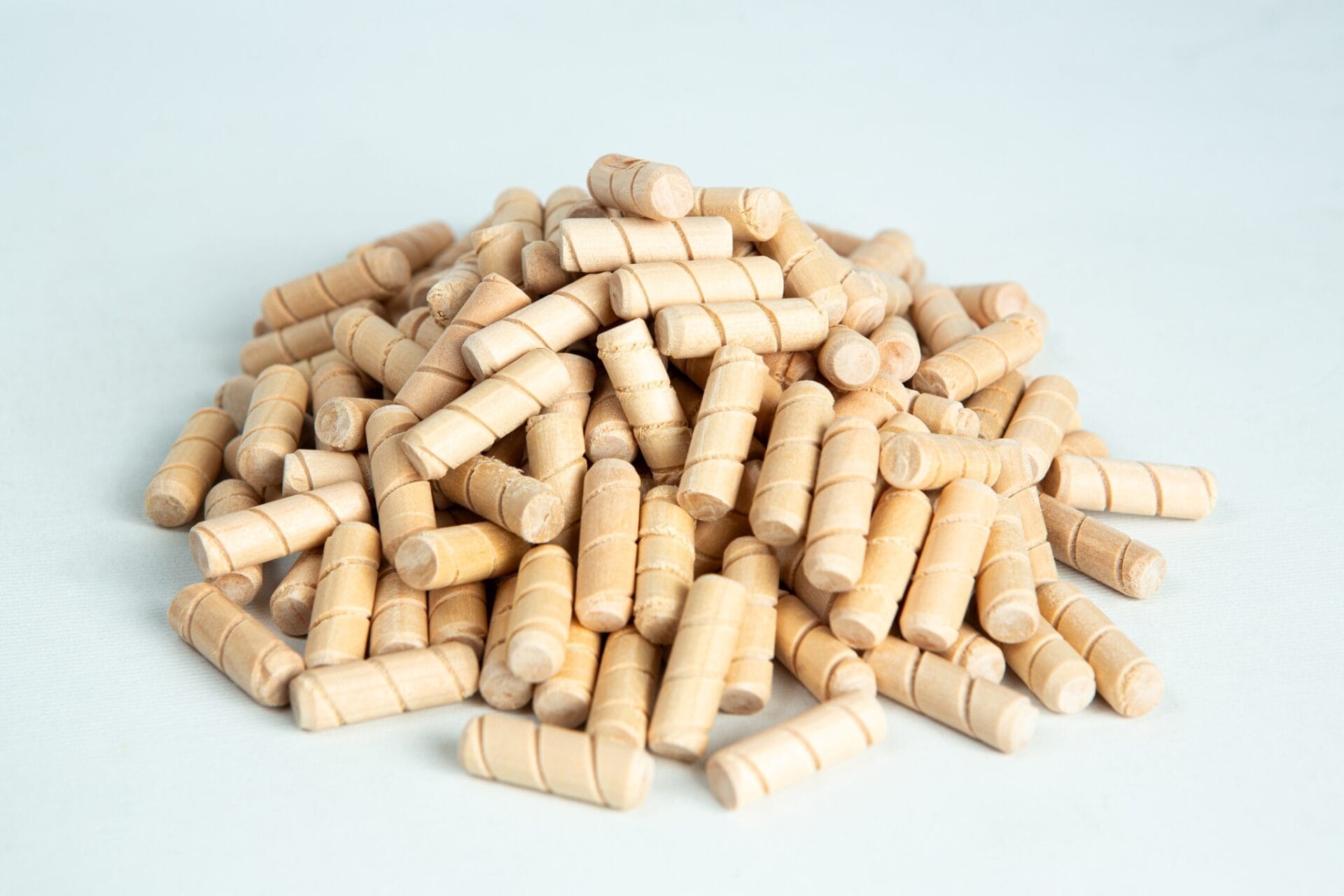 A pile of small, light wooden dowels on a white surface.