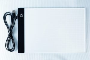 A USB cable and a flat, rectangular LED light pad for tracing on a white background.
