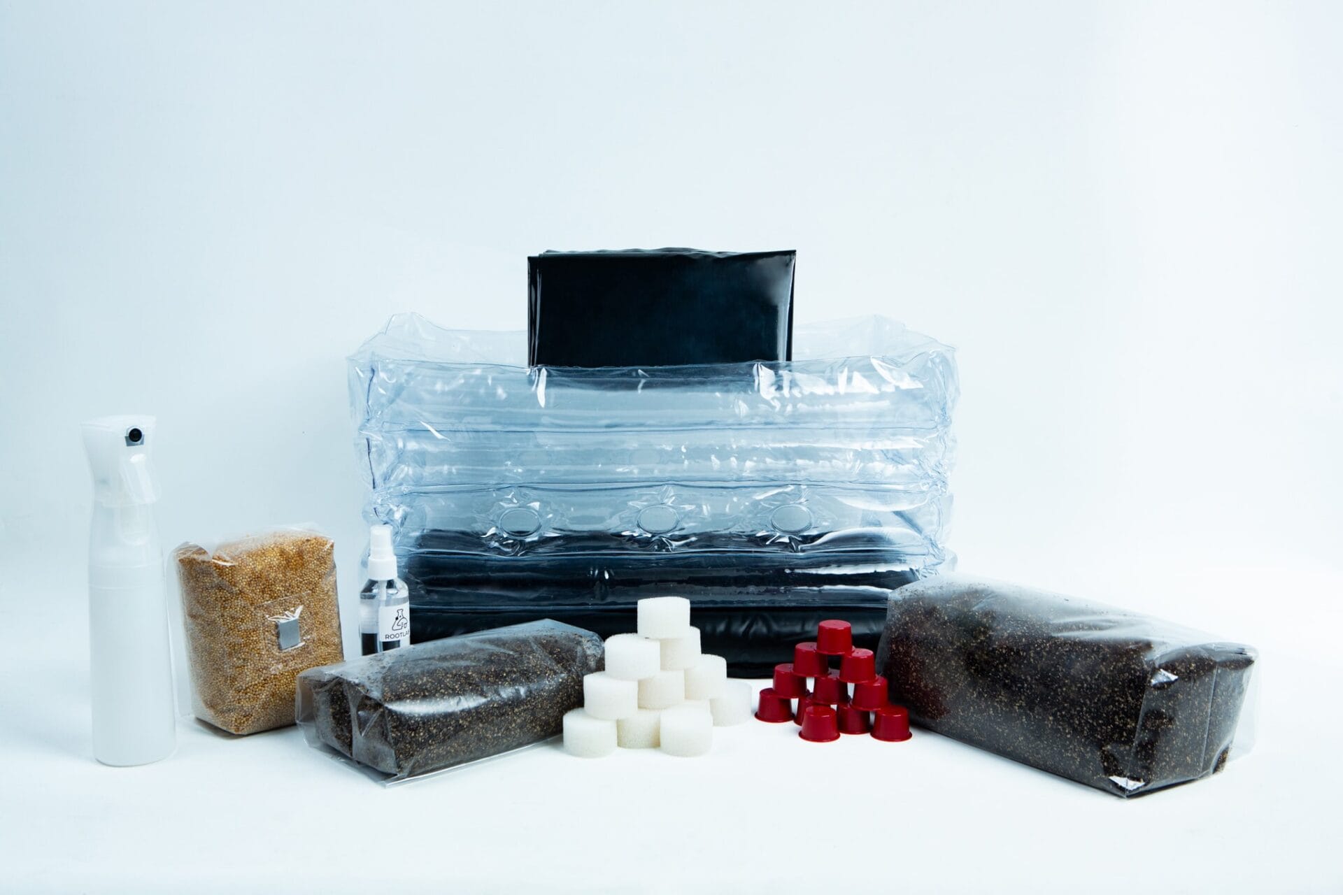 A mushroom growing kit with bags of substrate, a spray bottle, and small cubes on a white background.
