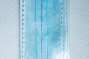 A Disposable Face Mask/Unit Individually wrapped in transparent plastic packaging is displayed on a light background.