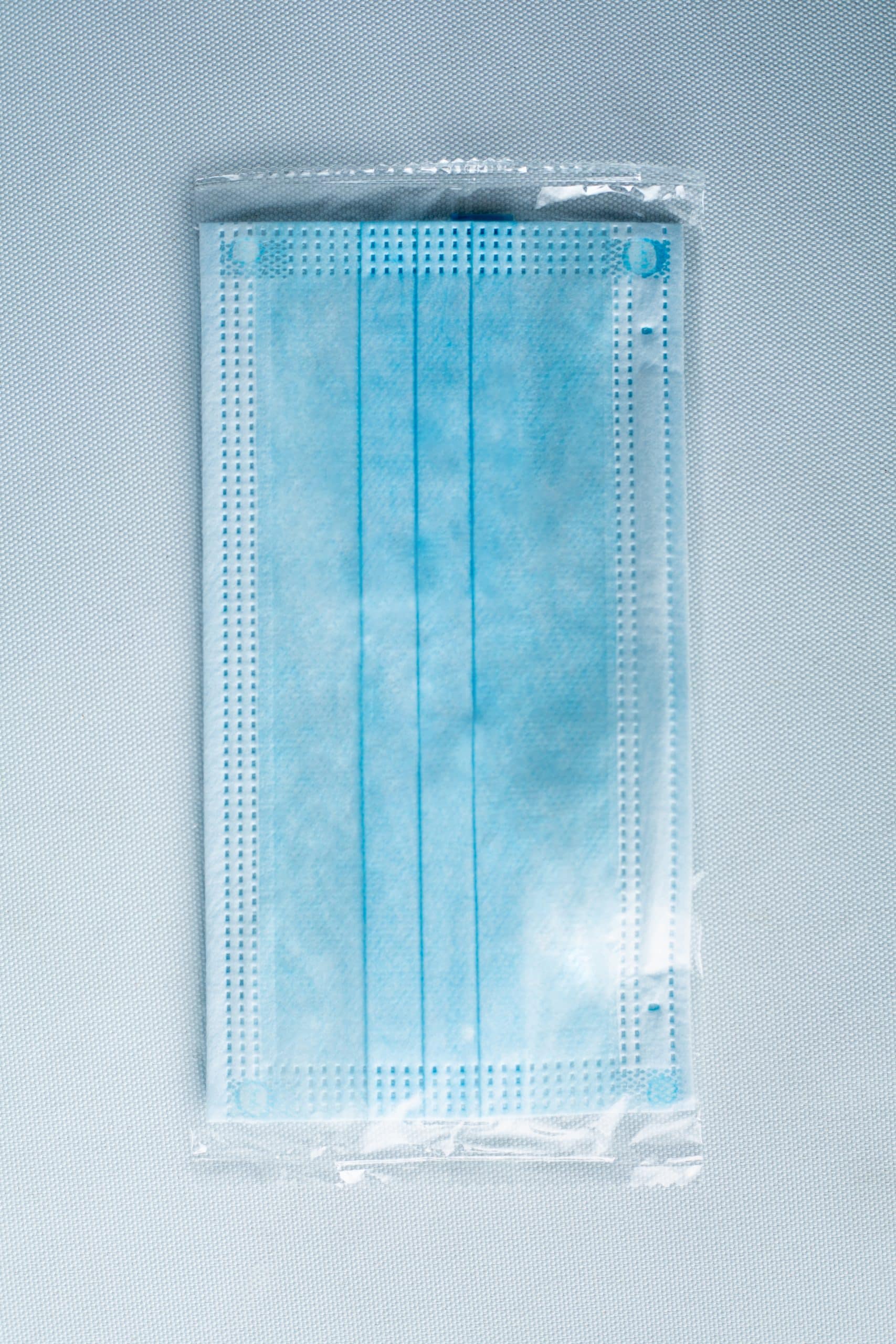 A Disposable Face Mask/Unit Individually wrapped in transparent plastic packaging is displayed on a light background.