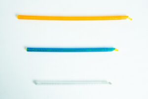 Three colourful twist ties, orange, blue, and clear, are laid out horizontally on a white background.