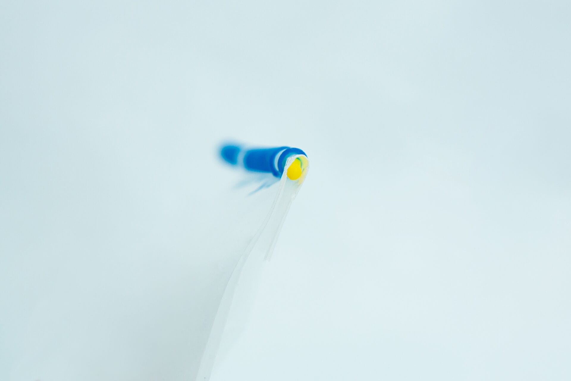 Close-up of a blue and yellow biro tip on a white background, with a shallow depth of field.