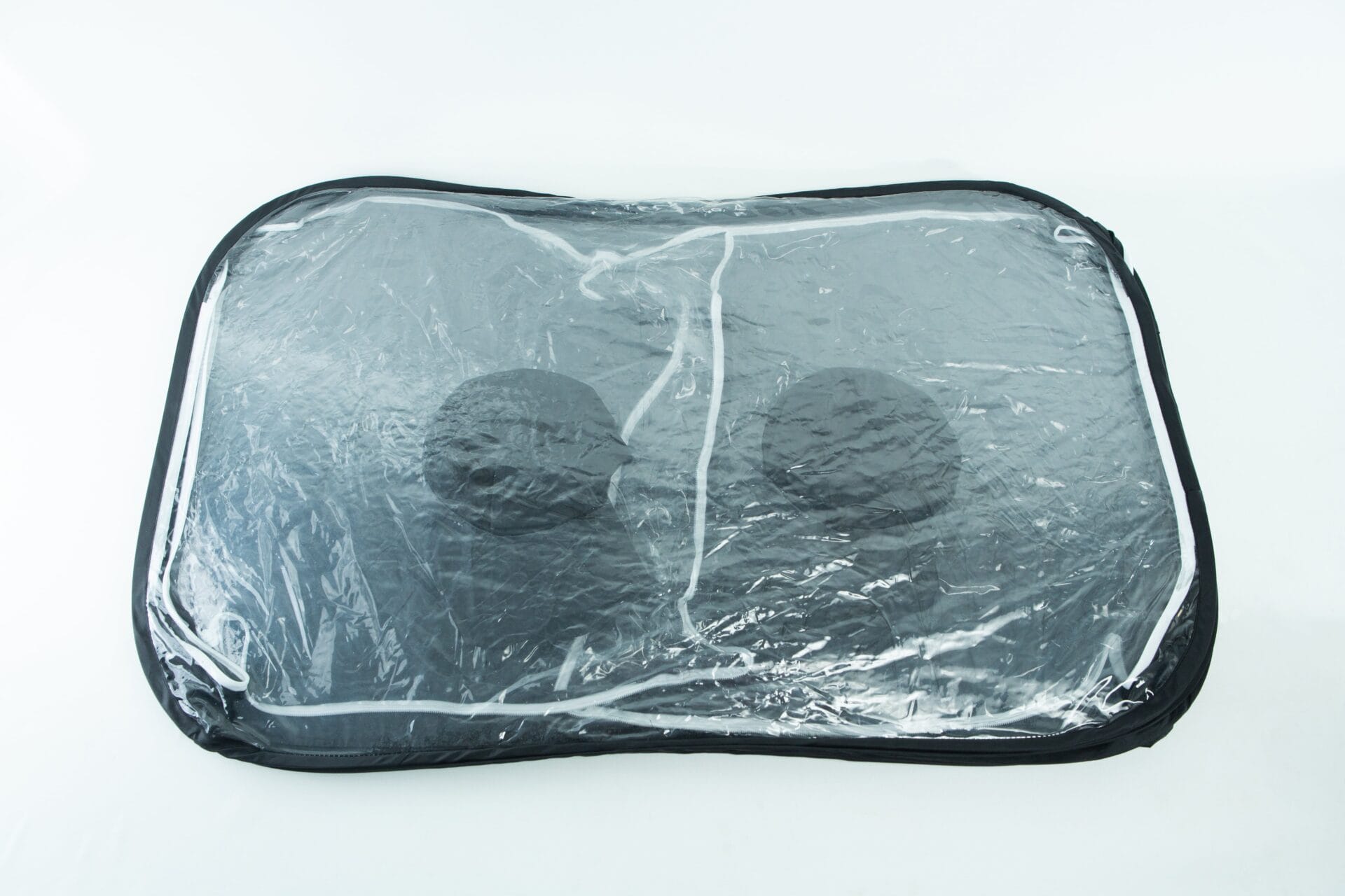 A transparent storage bag with black trim containing two black round objects.