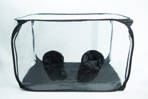 Clear pop-up box with two black fabric sleeves on the bottom panel, used for handling items inside safely.