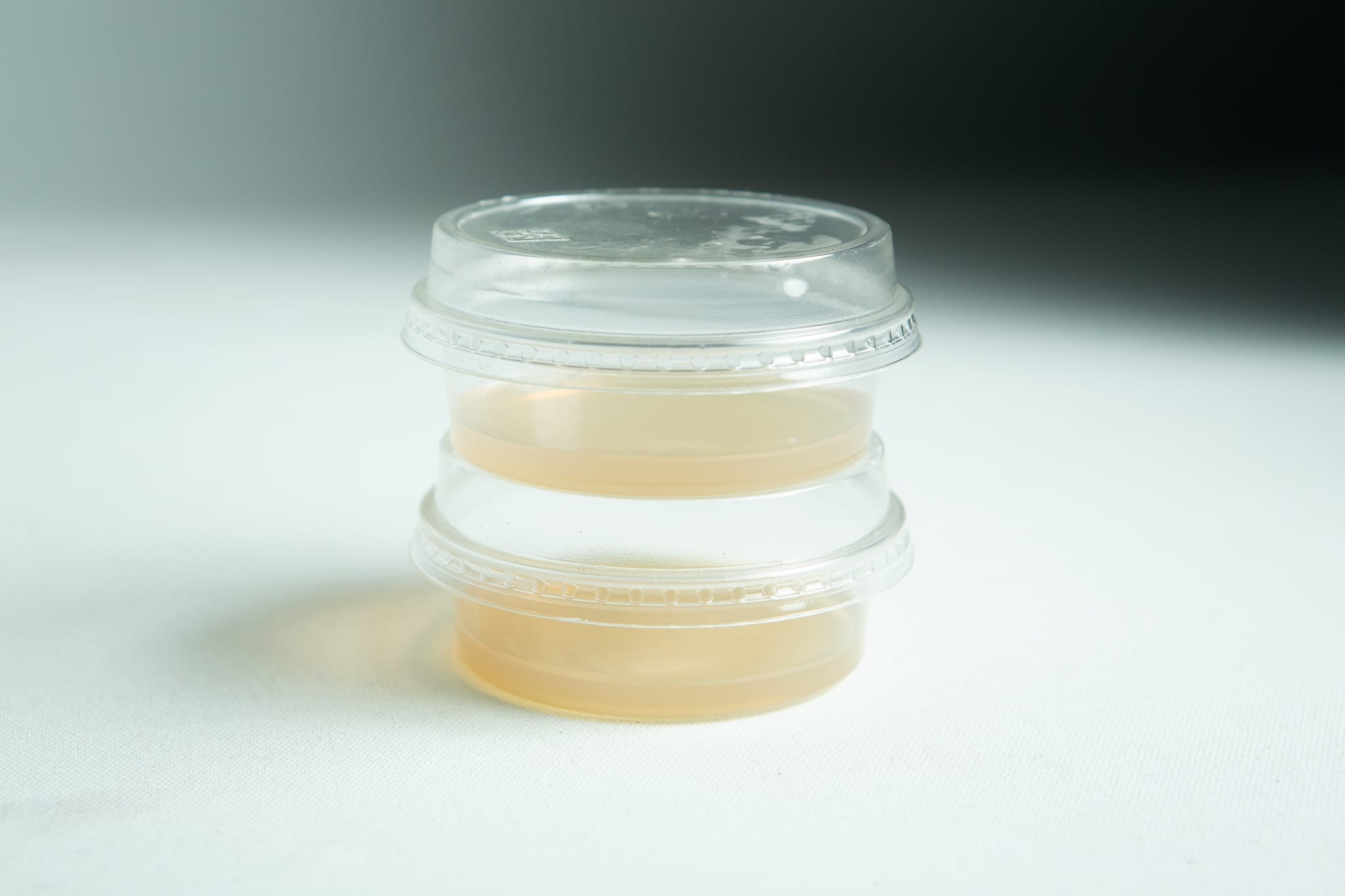 Two clear Biodegradable Agar Cups | MEA | MEAG are stacked, each containing a yellowish liquid, displayed against a white background.