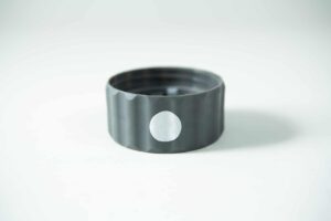 A Plant Cell Biocoupler™ Glass Set bottle cap—grey plastic with a white circular sticker on its side—rests on a white surface.