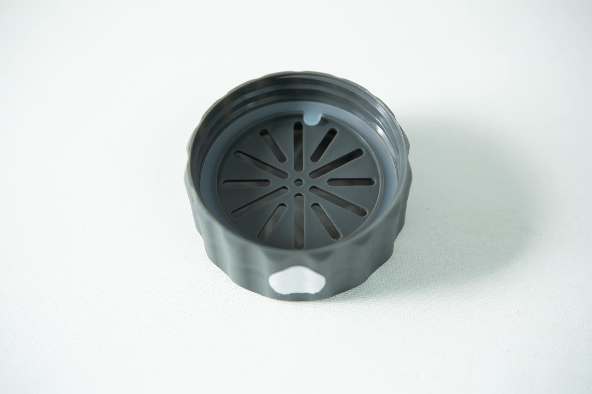 A black, round plastic lid with a slotted vent pattern, designed for the Plant Cell Biocoupler™ Glass Set (16oz, 12oz, 8oz), is shown on a white surface.