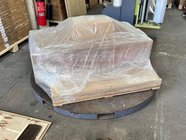 A pallet wrapped in clear plastic sits on a large metal platform in a warehouse, positioned near a Laminar Flow Hood H14 with prefilter 120x60x35cm to ensure optimal air quality.