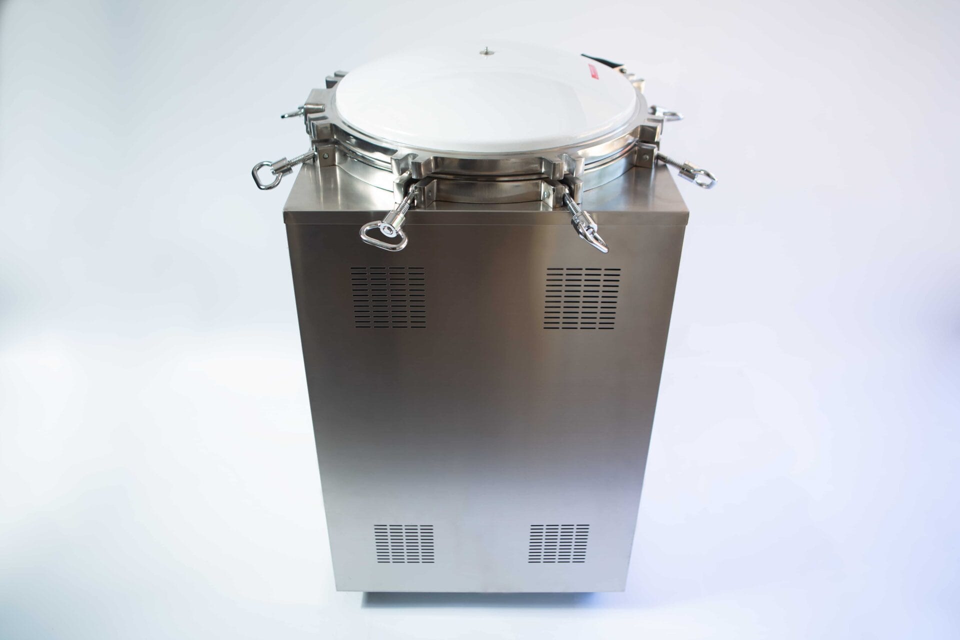 A stainless steel autoclave machine with a round, sealed lid and catches on a plain background.