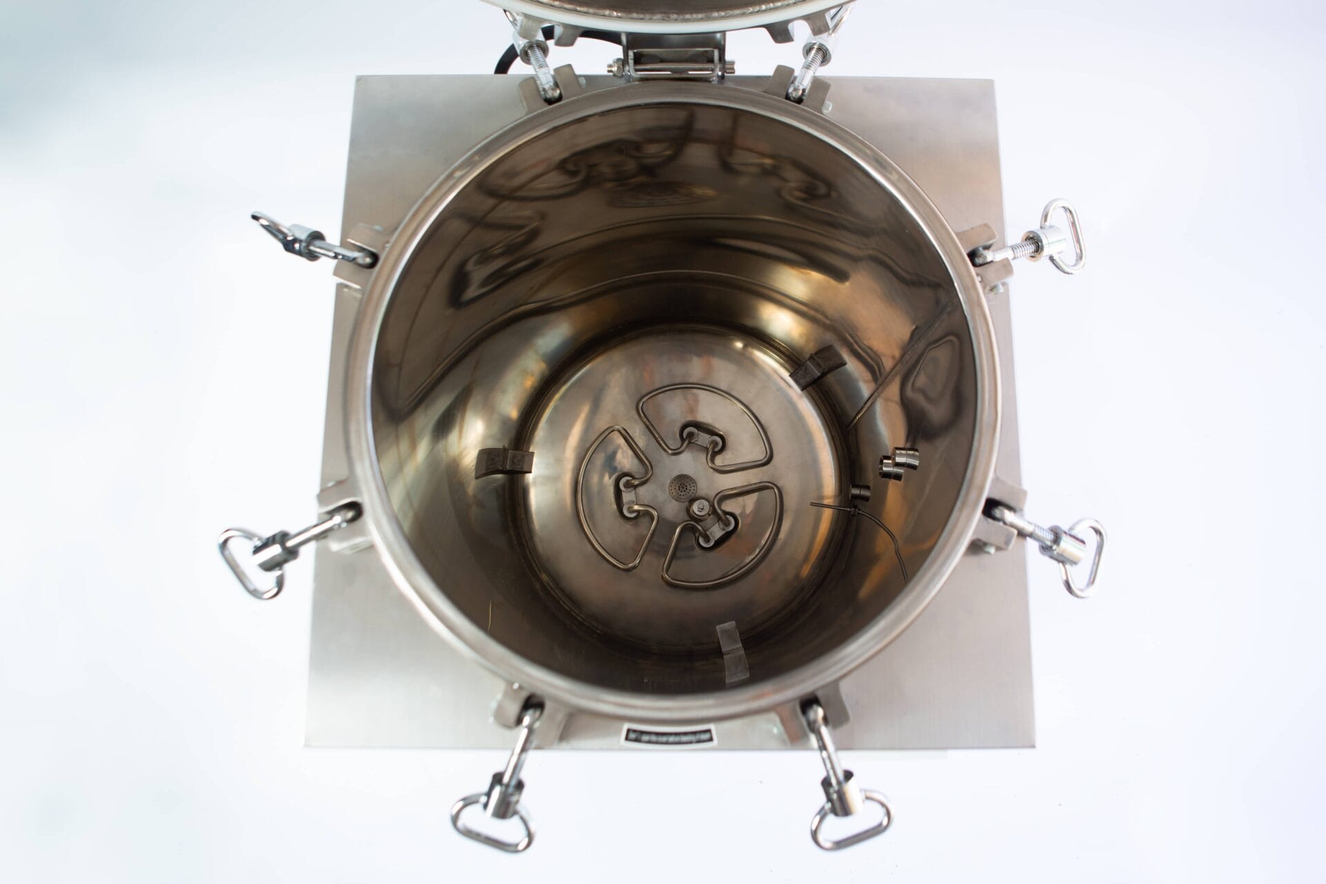 Top-down view of an open stainless steel industrial mixing or processing vessel with clamps around the edge.