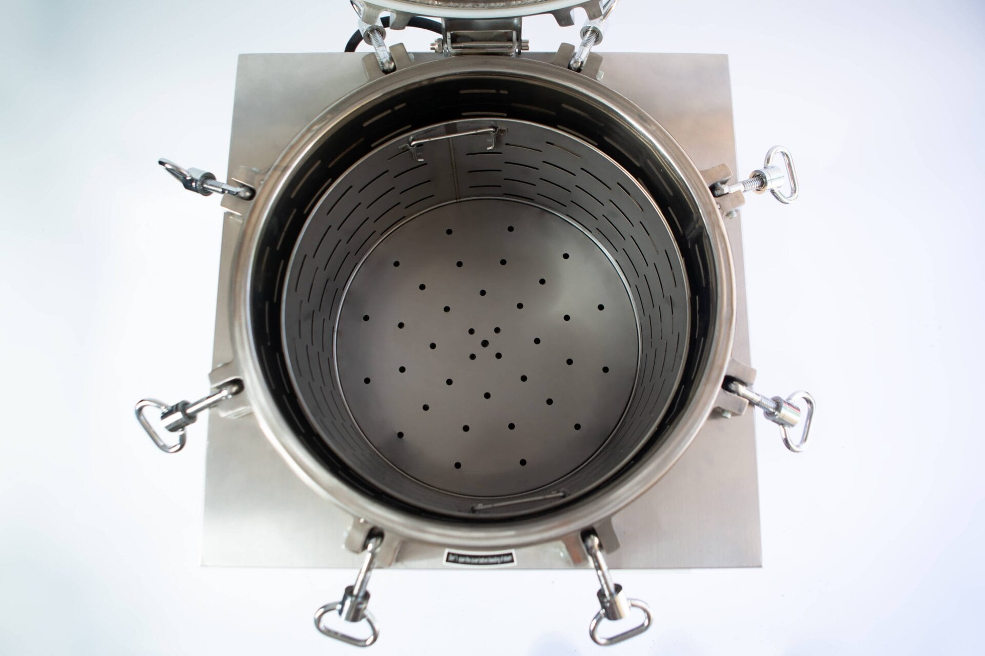 Top view of an open stainless steel industrial container with a perforated plate inside.