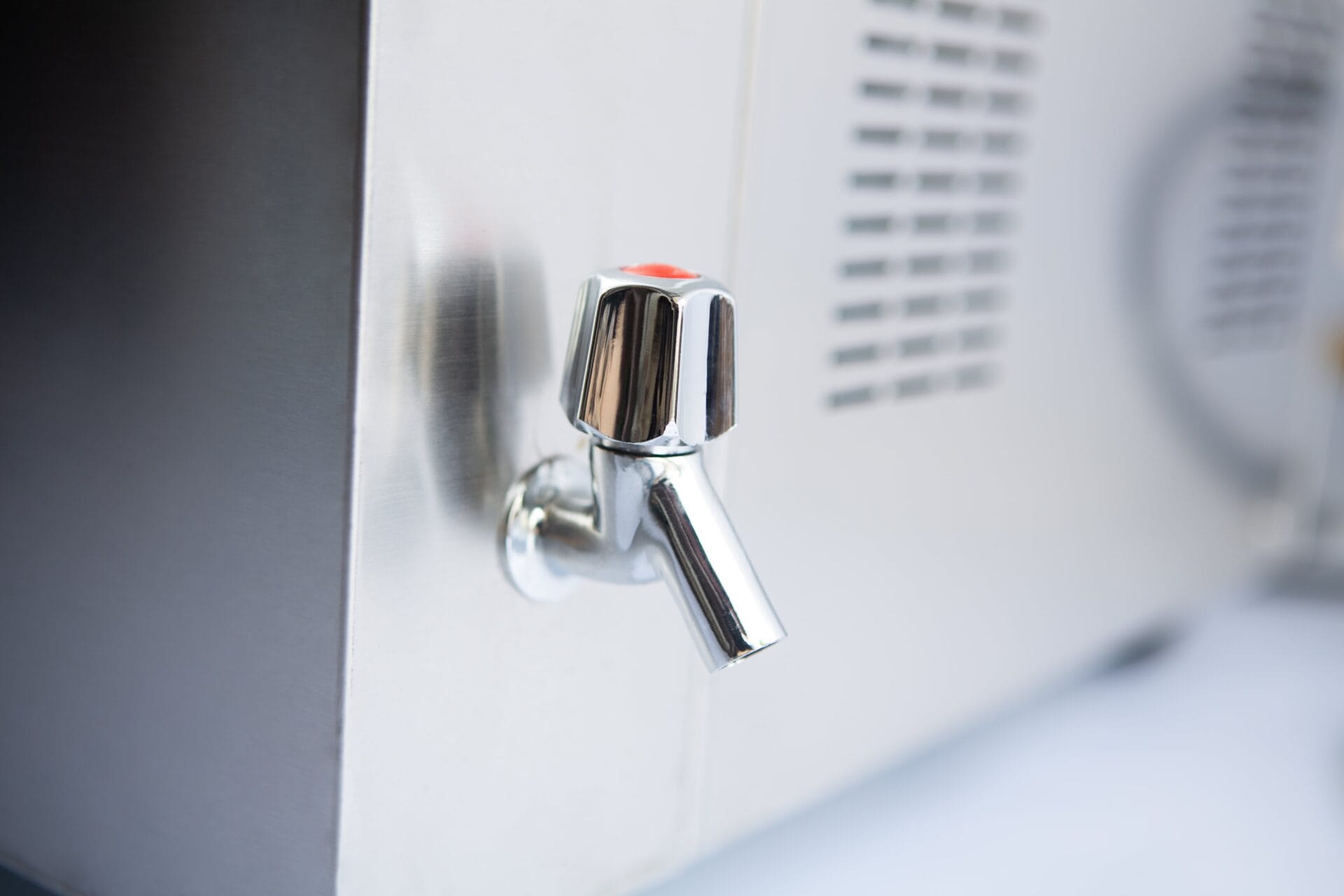 Close-up of a shiny metal water tap attached to a stainless steel appliance or dispenser.