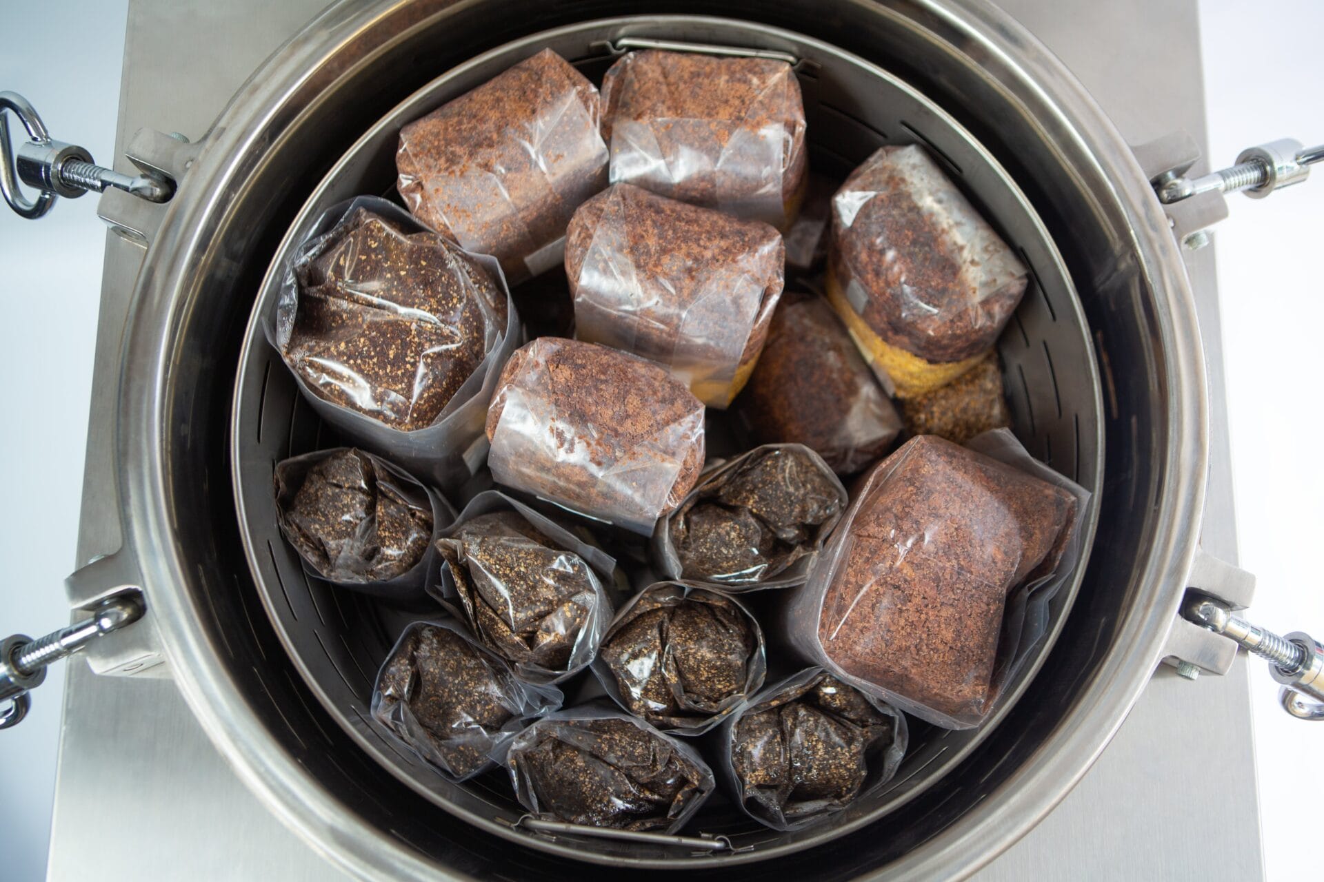 Plastic bags filled with a brown substrate inside a metal container, likely for mushroom cultivation.
