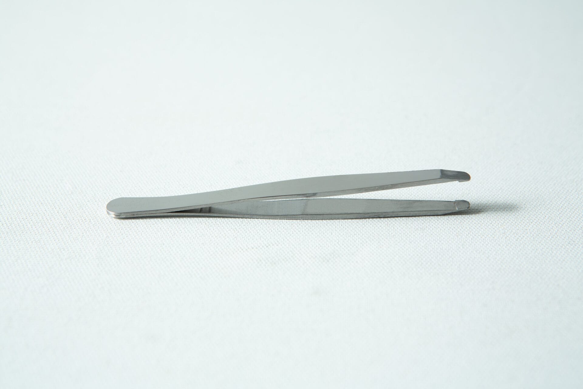 A pair of metal tweezers rests on a white surface, ideal for use with your slime mould kit - Physarum polycephalum.