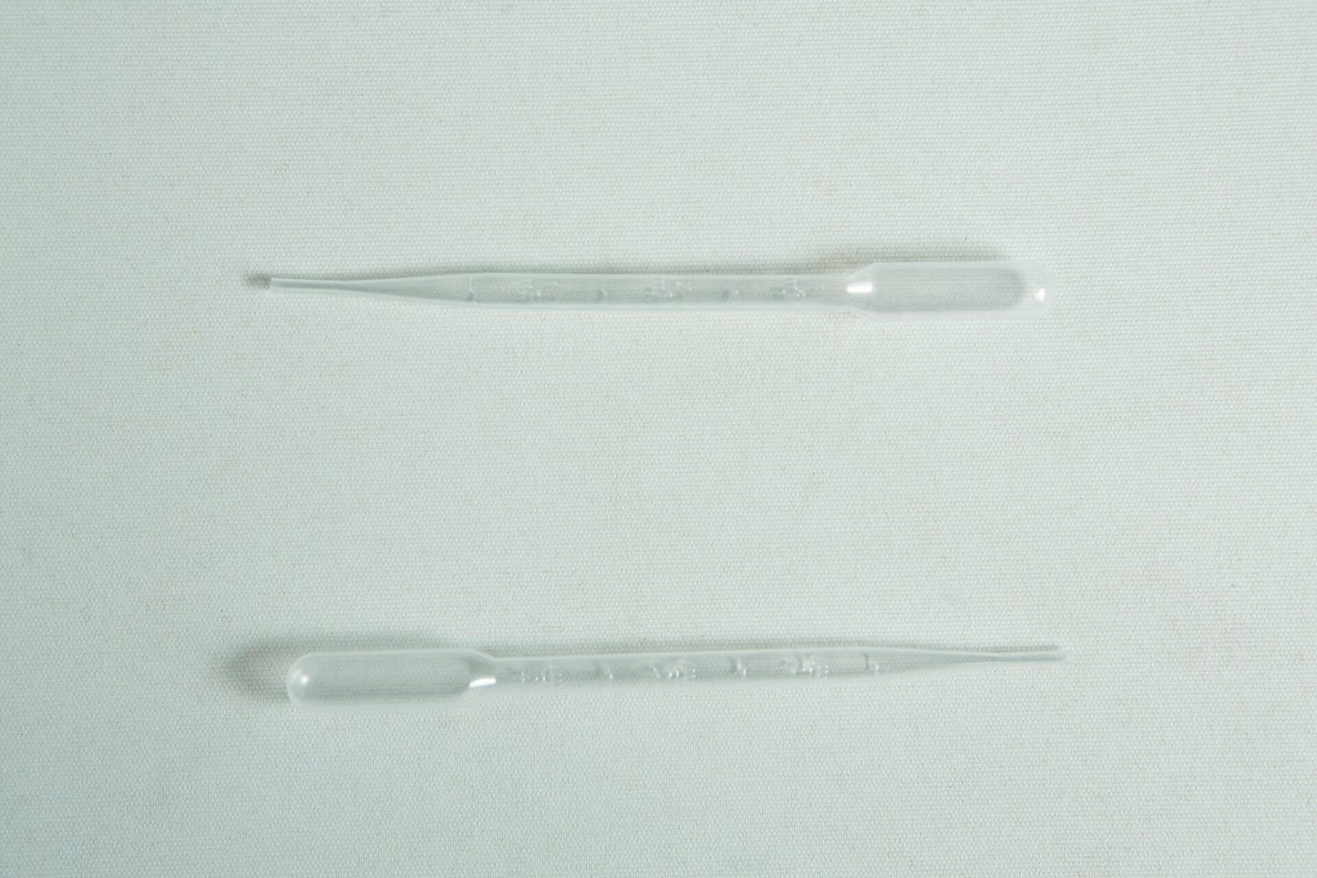 Two clear plastic pipettes from the Plantcell Synthetic Seed Starter Kit lie parallel on a light, textured surface.