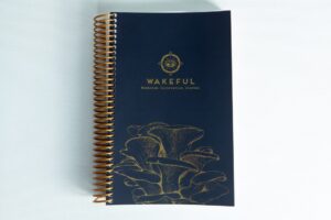 Dark blue spiral-bound Wakeful Mushroom Cultivation Journal by Australian mycologist Caine Barlow, featuring gold mushrooms on the cover.