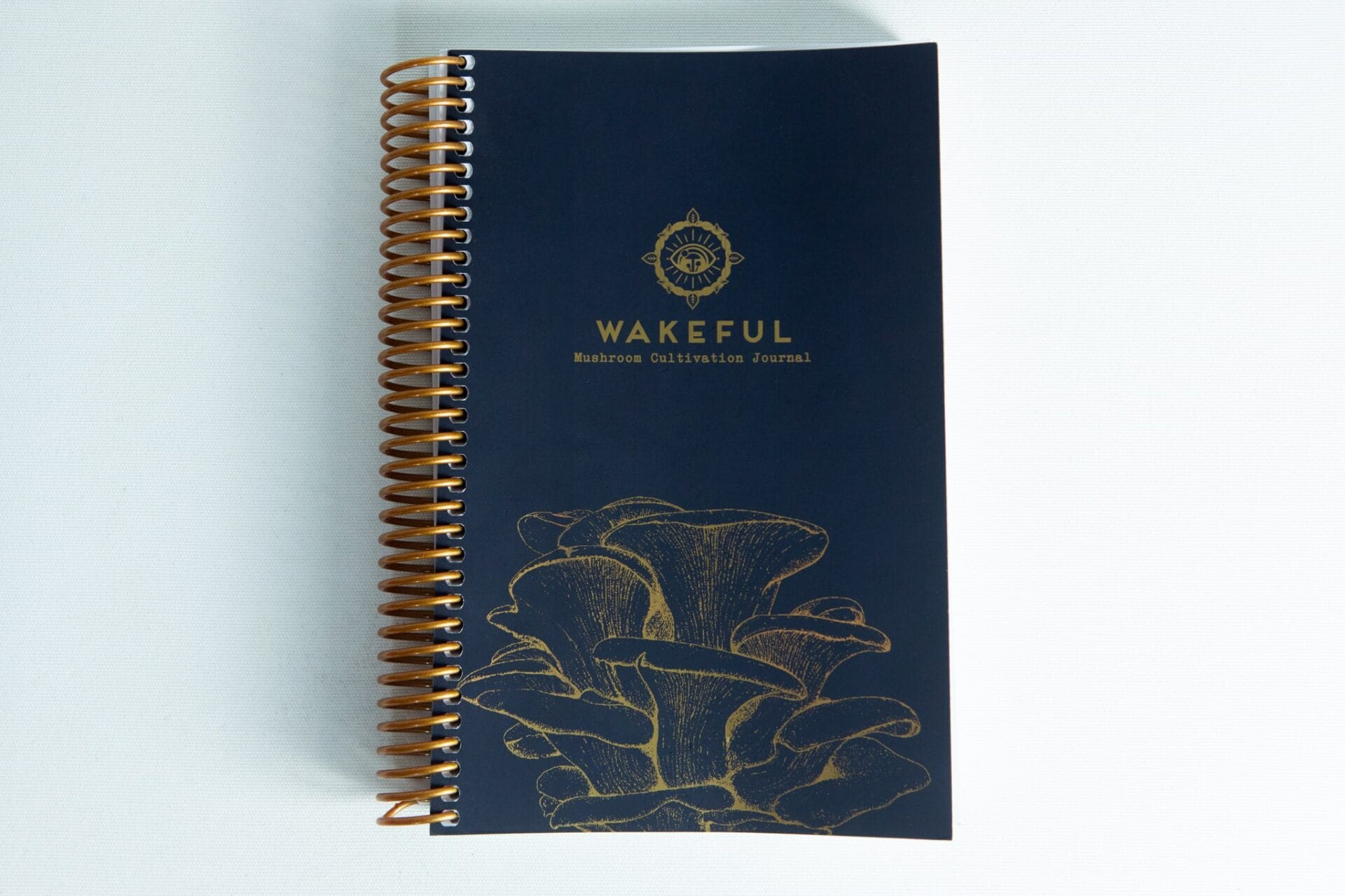 Dark blue spiral-bound Wakeful Mushroom Cultivation Journal by Australian mycologist Caine Barlow, featuring gold mushrooms on the cover.