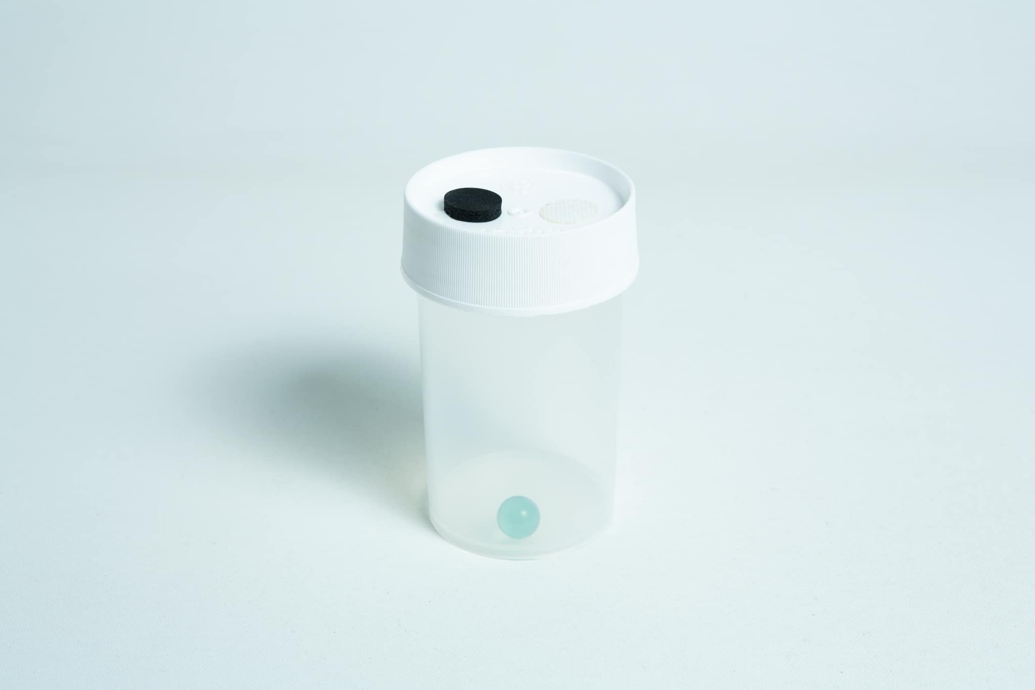 The Liquid Culture to Liquid Culture Expansion Kit features a clear plastic container with a white lid, black button, and a small blue sphere inside.