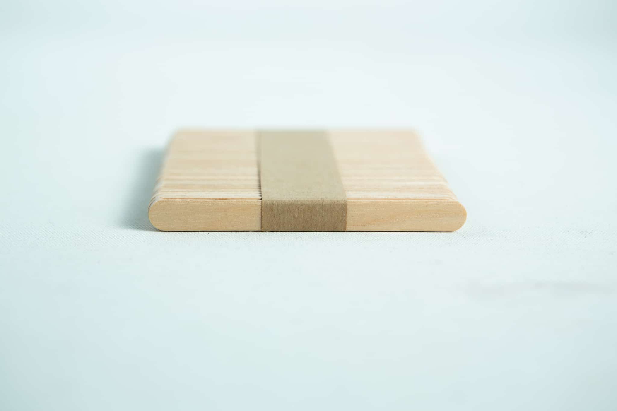 A stack of ice lolly sticks, neatly bundled with a brown paper band, is arranged on a white surface.