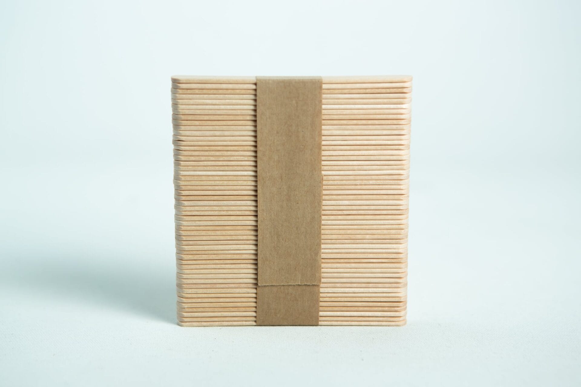 A bundle of ice lolly sticks, neatly wrapped with a brown paper band, is set against a white background.